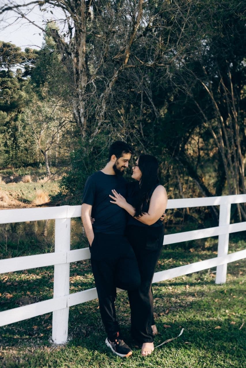Camila e Bernardo sorrindo juntos junto a uma cerca branca